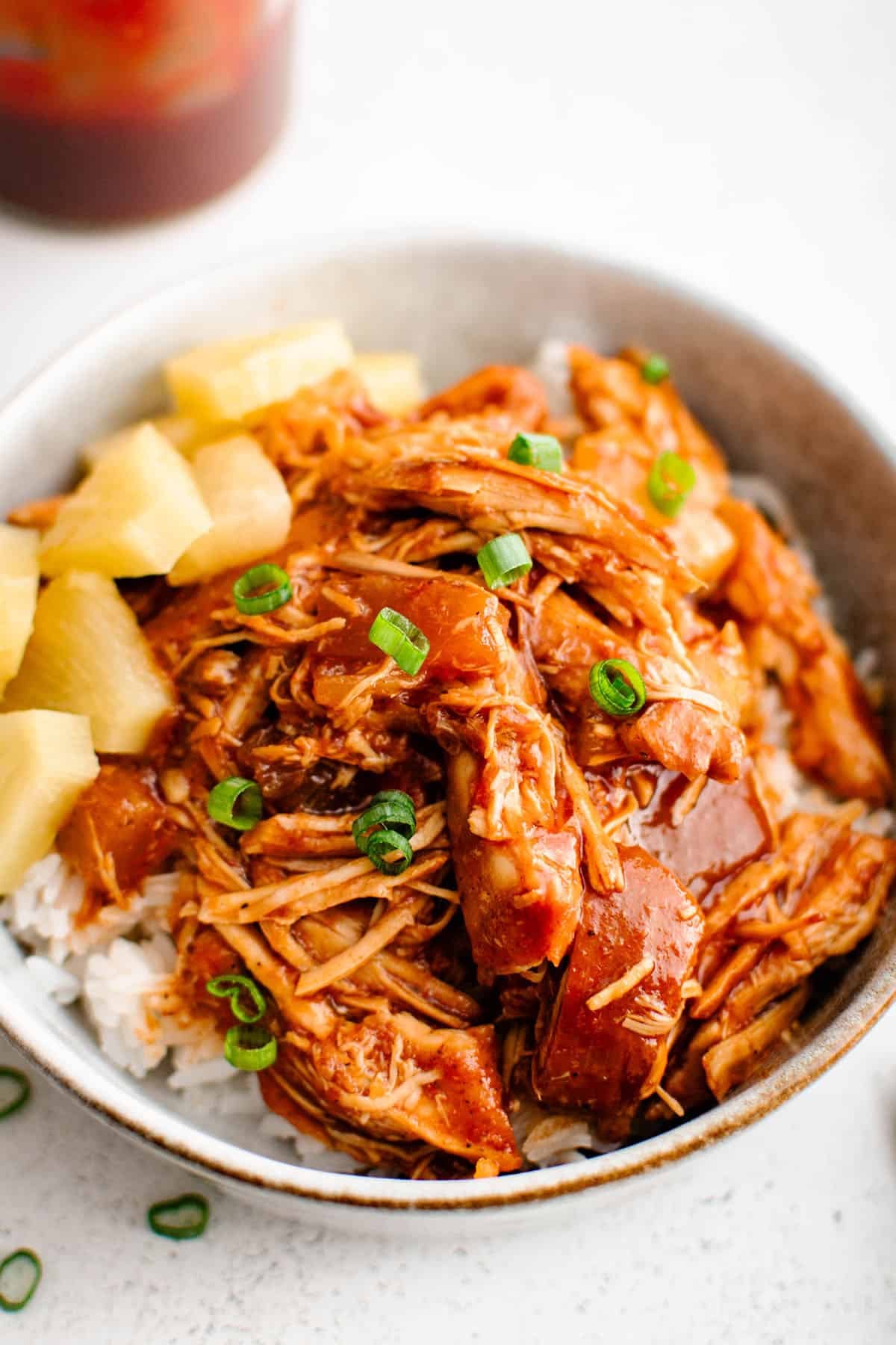 Crockpot Pineapple BBQ Chicken in a bowl topped with pineapple chunks and garnished with sliced green onions