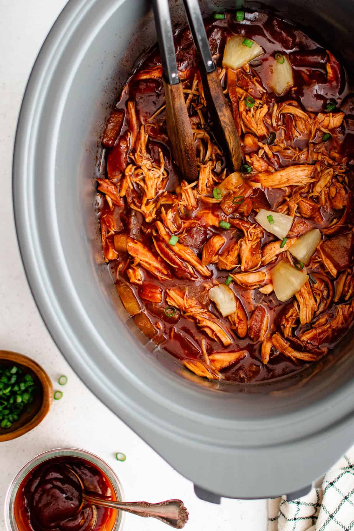 crockpot pineapple bbq chicken in a crockpot with a pair tongs resting on top