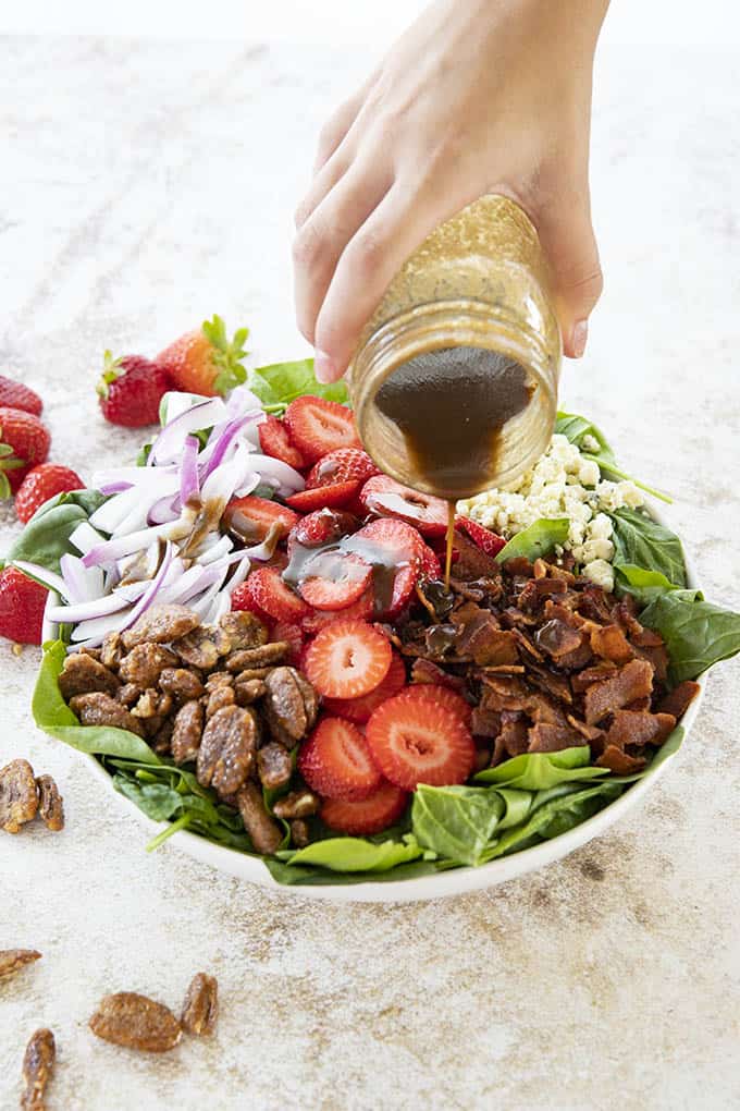 pouring dressing on strawberry spinach salad