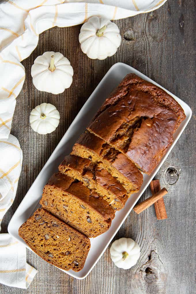 top view of sliced pumpkin bread loaf with white mini pumpkins