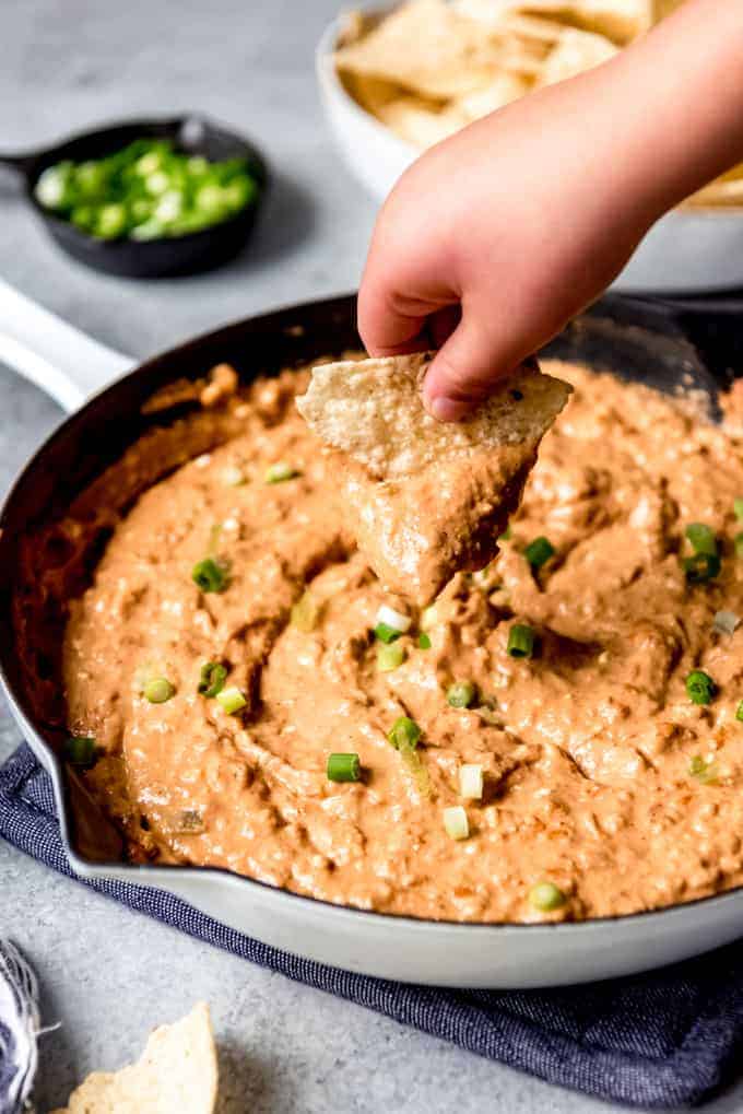 An image of a hand holding a chip to scoop bean dip.