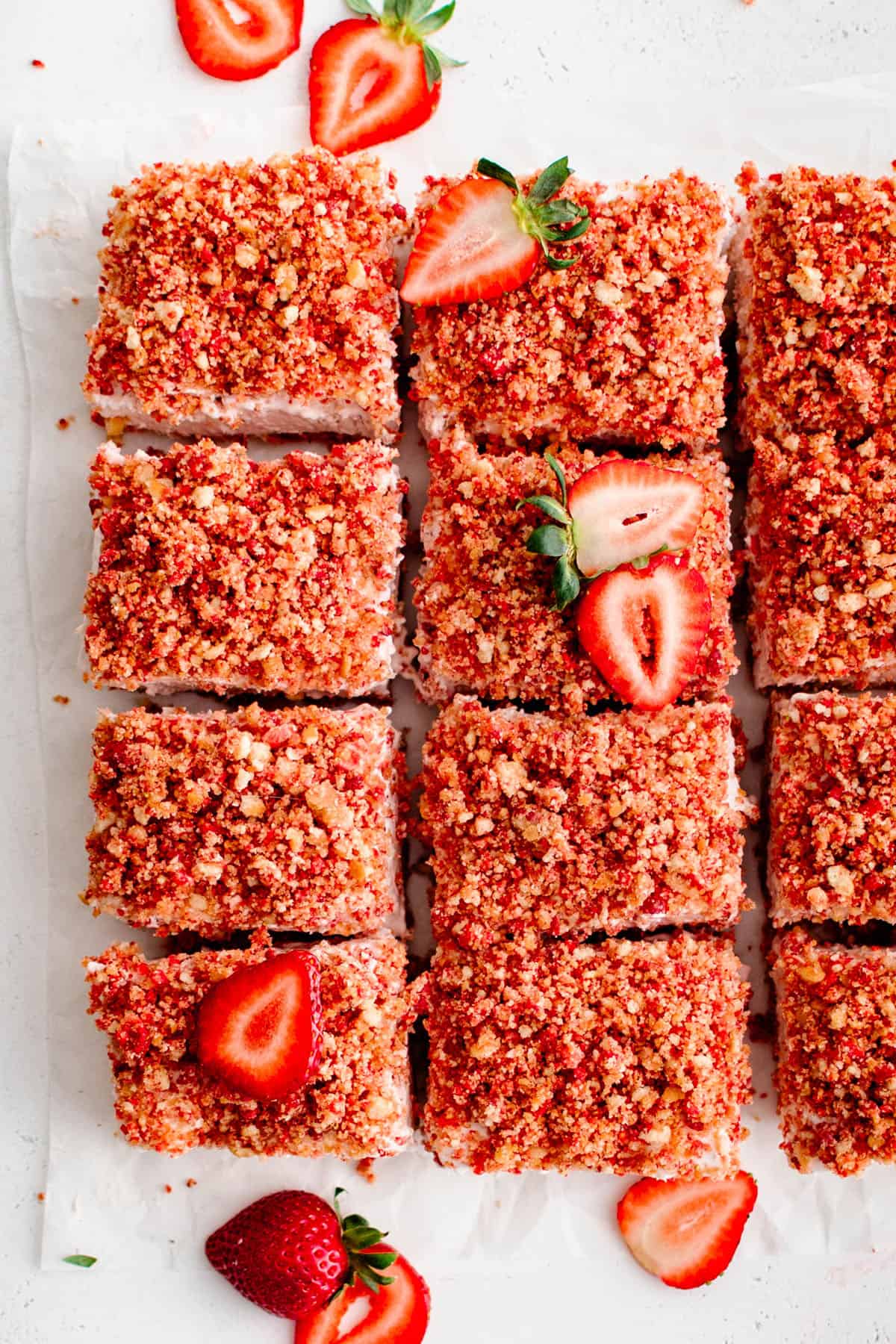 overhead photo of strawberry cheesecake bars cut into individual pieces, with fresh sliced strawberries as a garnish