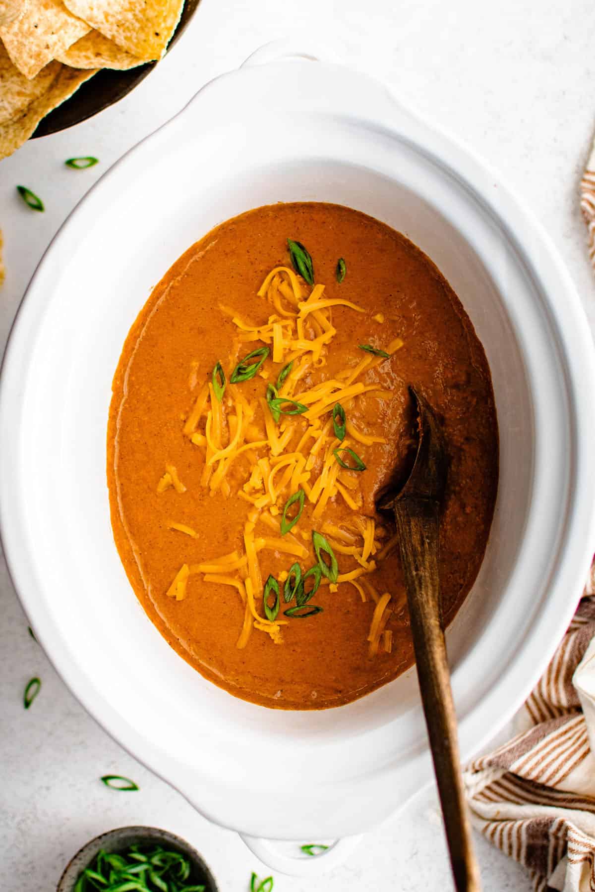 chili cheese dip in a crockpot with a wooden spoon and a green onion garnish