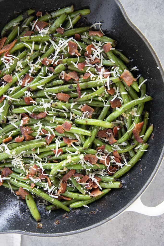 skillet with green beans topped with bacon and parmesan cheese