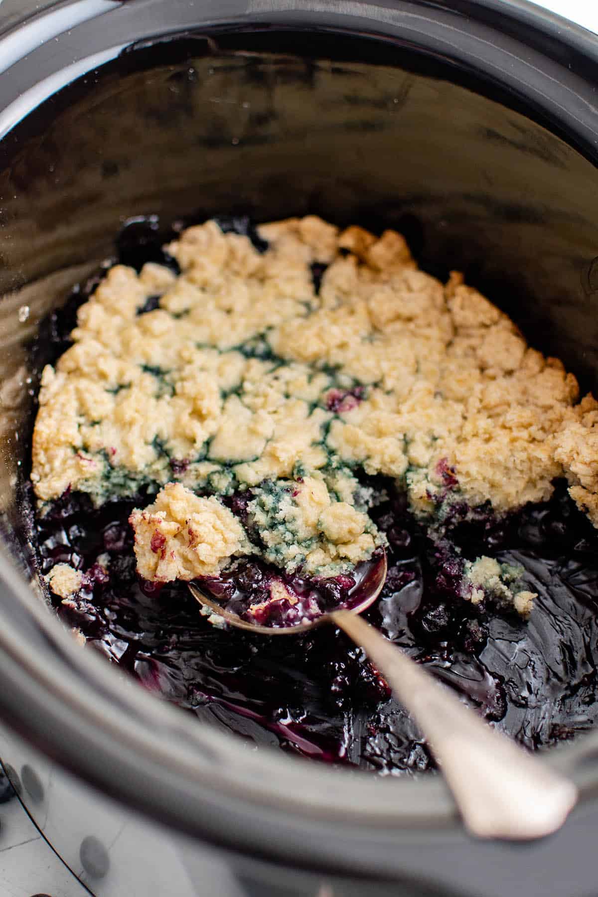 Blueberry Cobbler in a slow cooker with a spoon resting in it