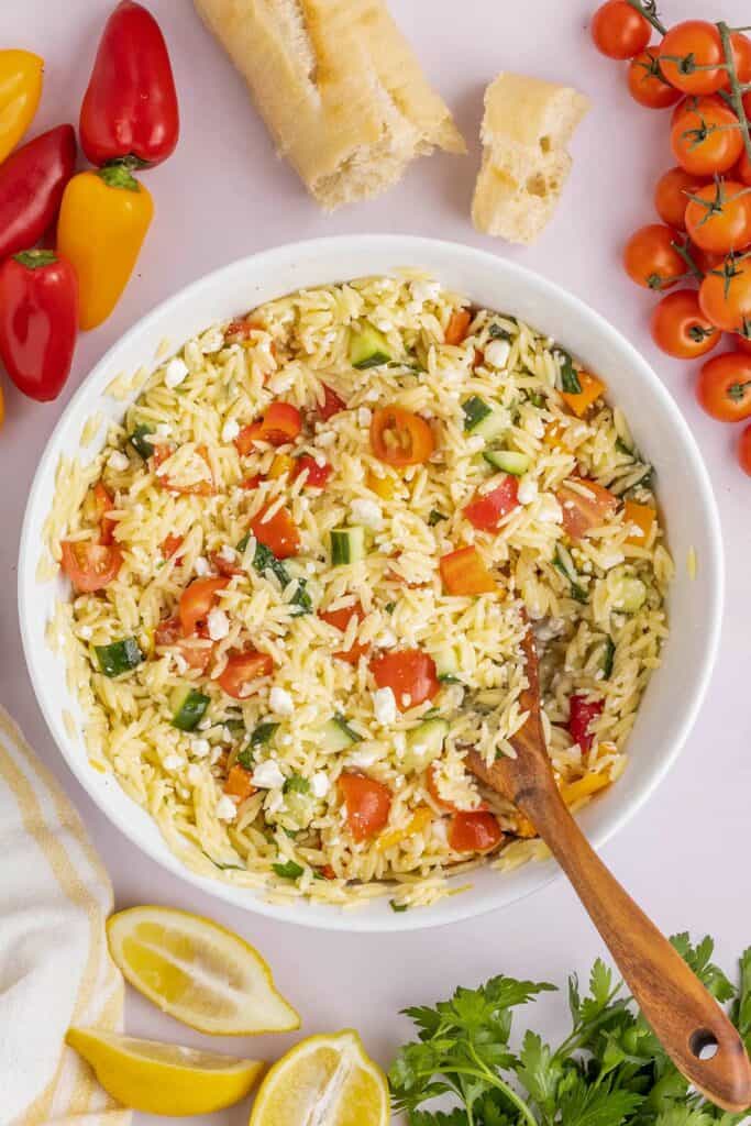orzo salad in a bowl with a wooden spoon