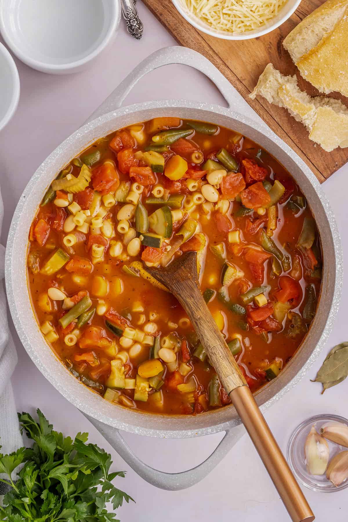 Overhead image of a pot of prepared minestrone soup with a wooden spoon in it