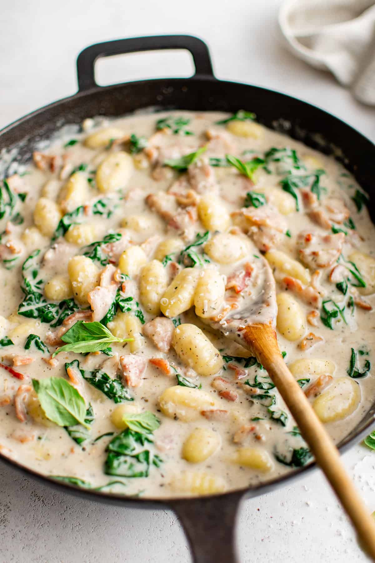 creamy gnocchi with bacon in a skillet with wooden spoon