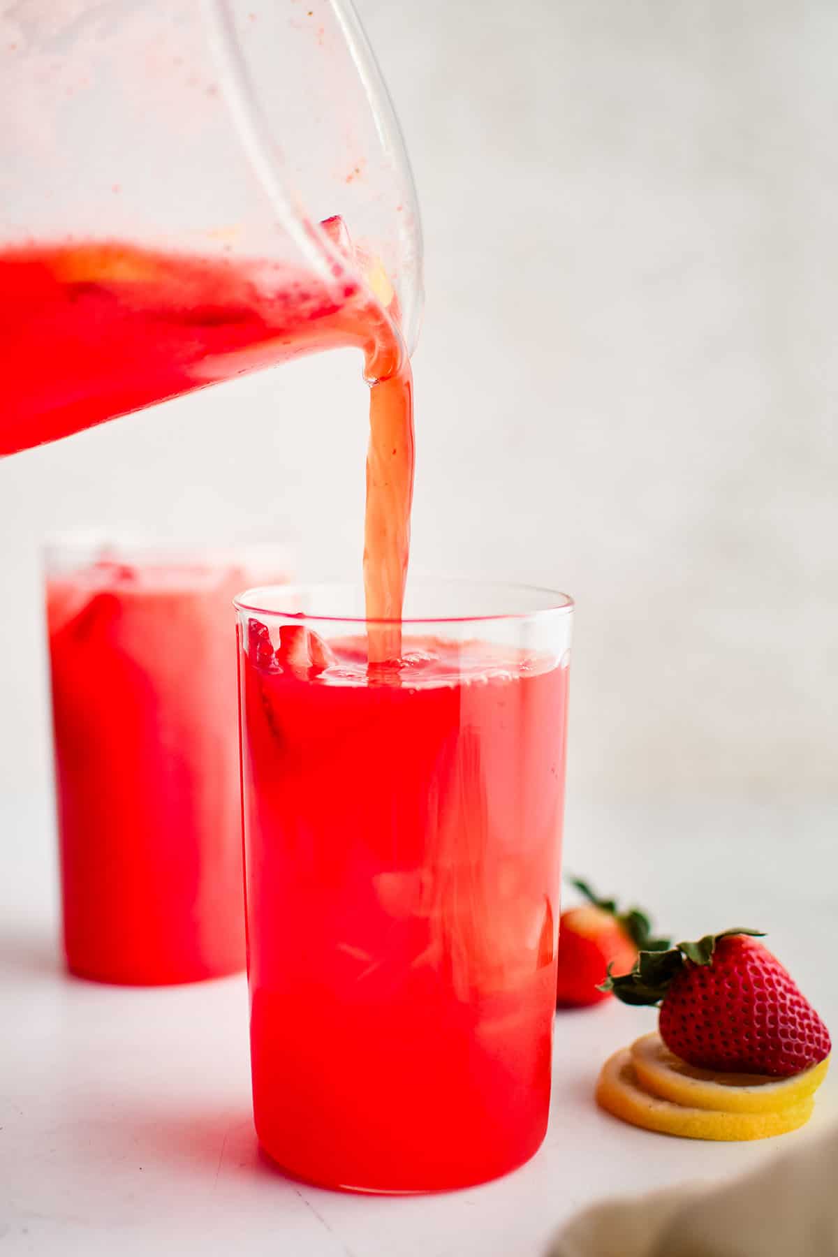 strawberry lemonade being poured from a pitcher into a glass