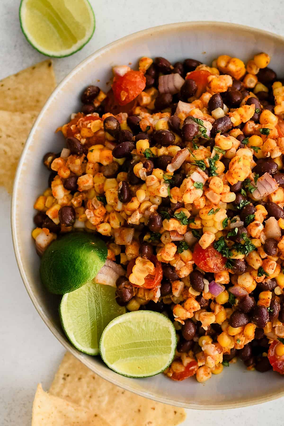 corn and black bean salad in a white bowl with limes