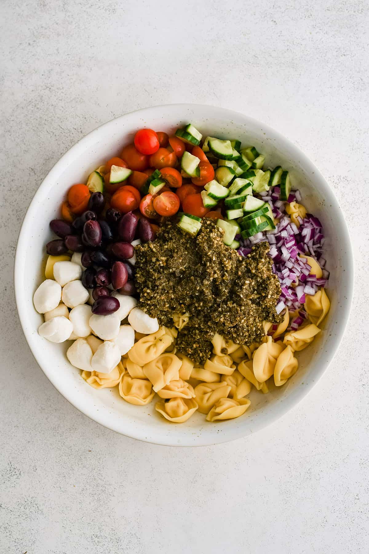ingredients to make pesto tortellini salad in a large bowl