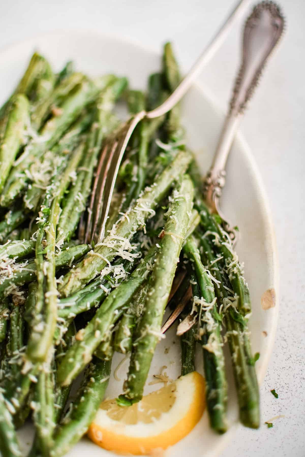 roasted green beans in a white serving dish with parmesan and lemon