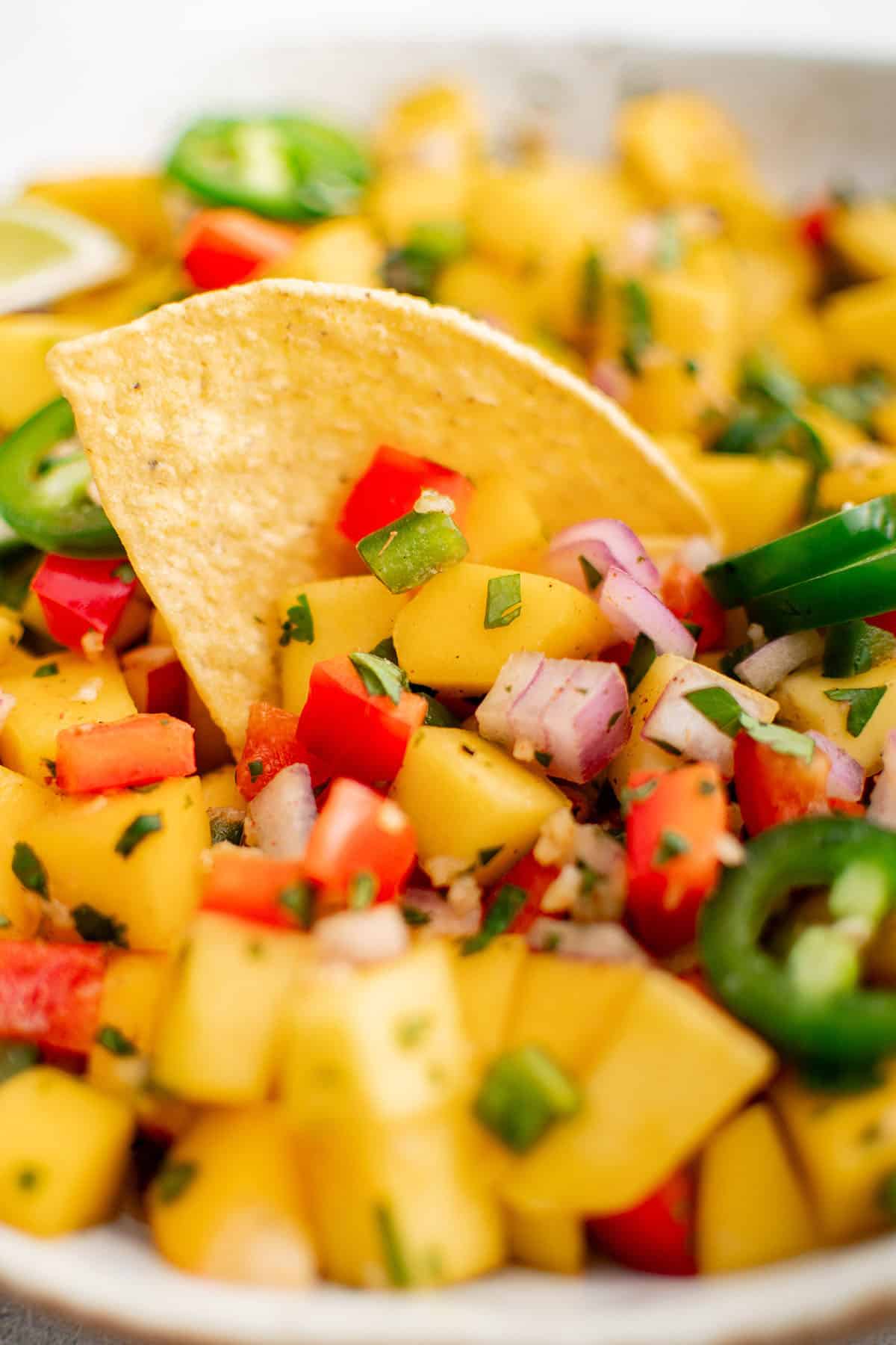 mango salsa in a white bowl with a chip