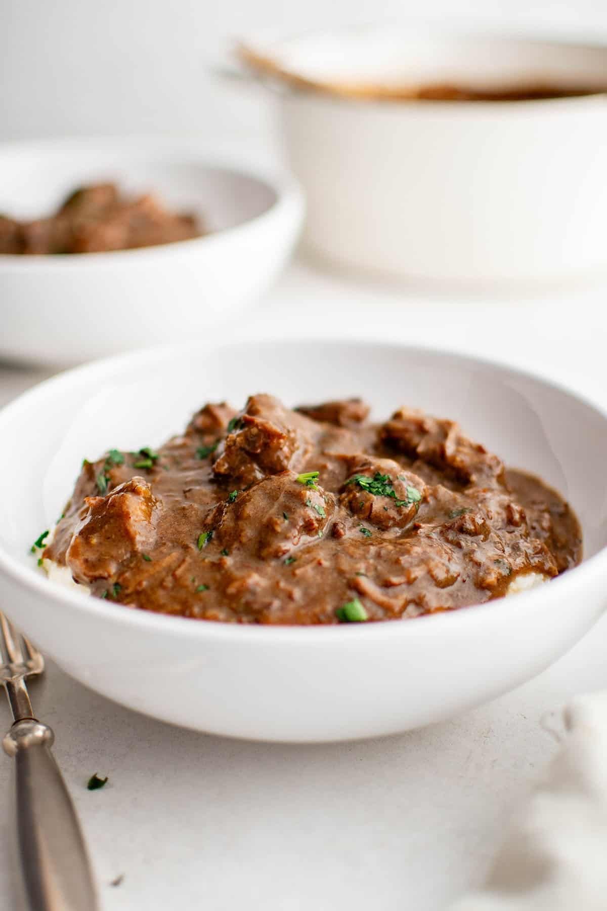 beef tips and gravy in a white bowl with mashed potatoes