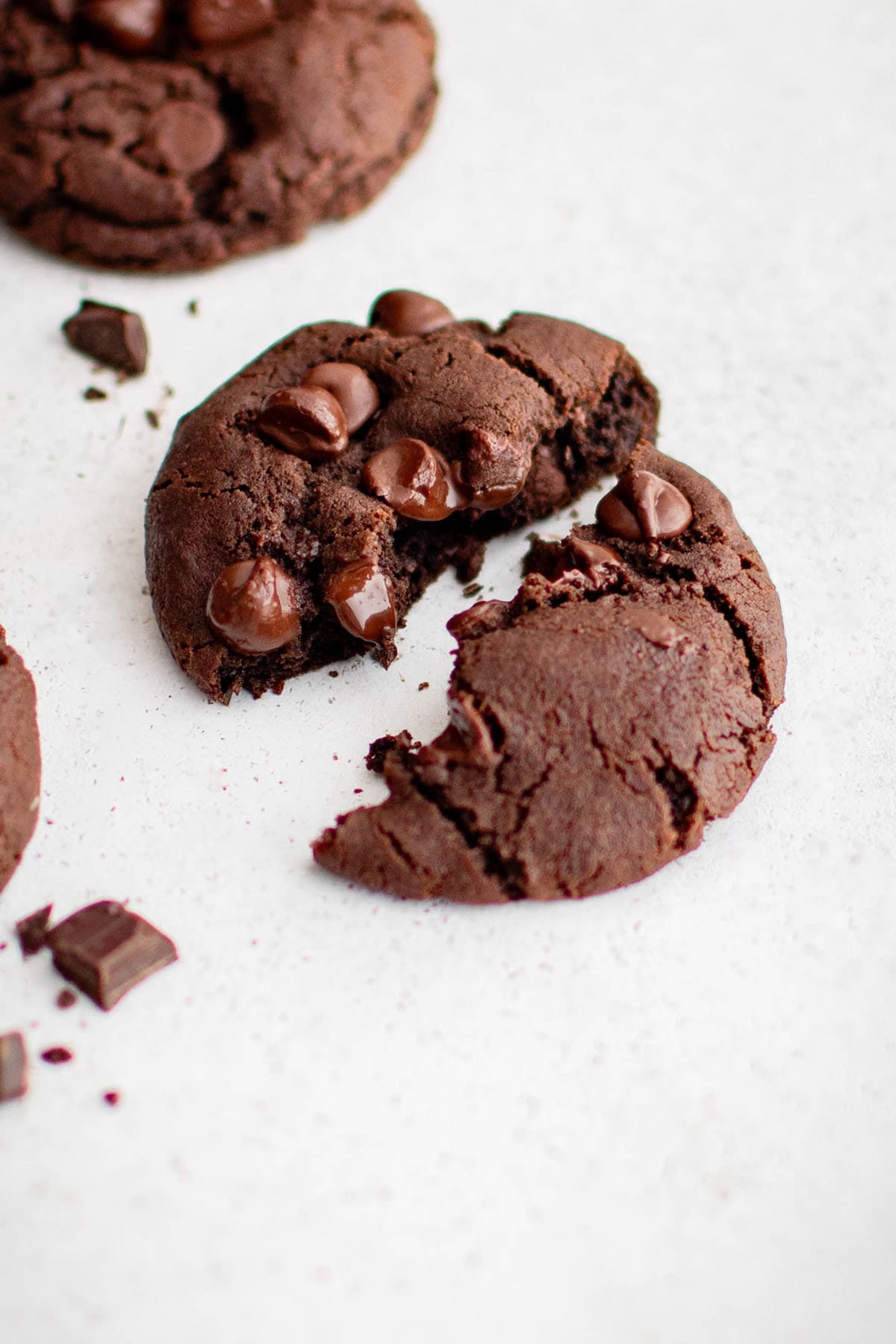 a chocolate cookie broken in half, with melty chocolate chips on top and a gooey texture in the middle