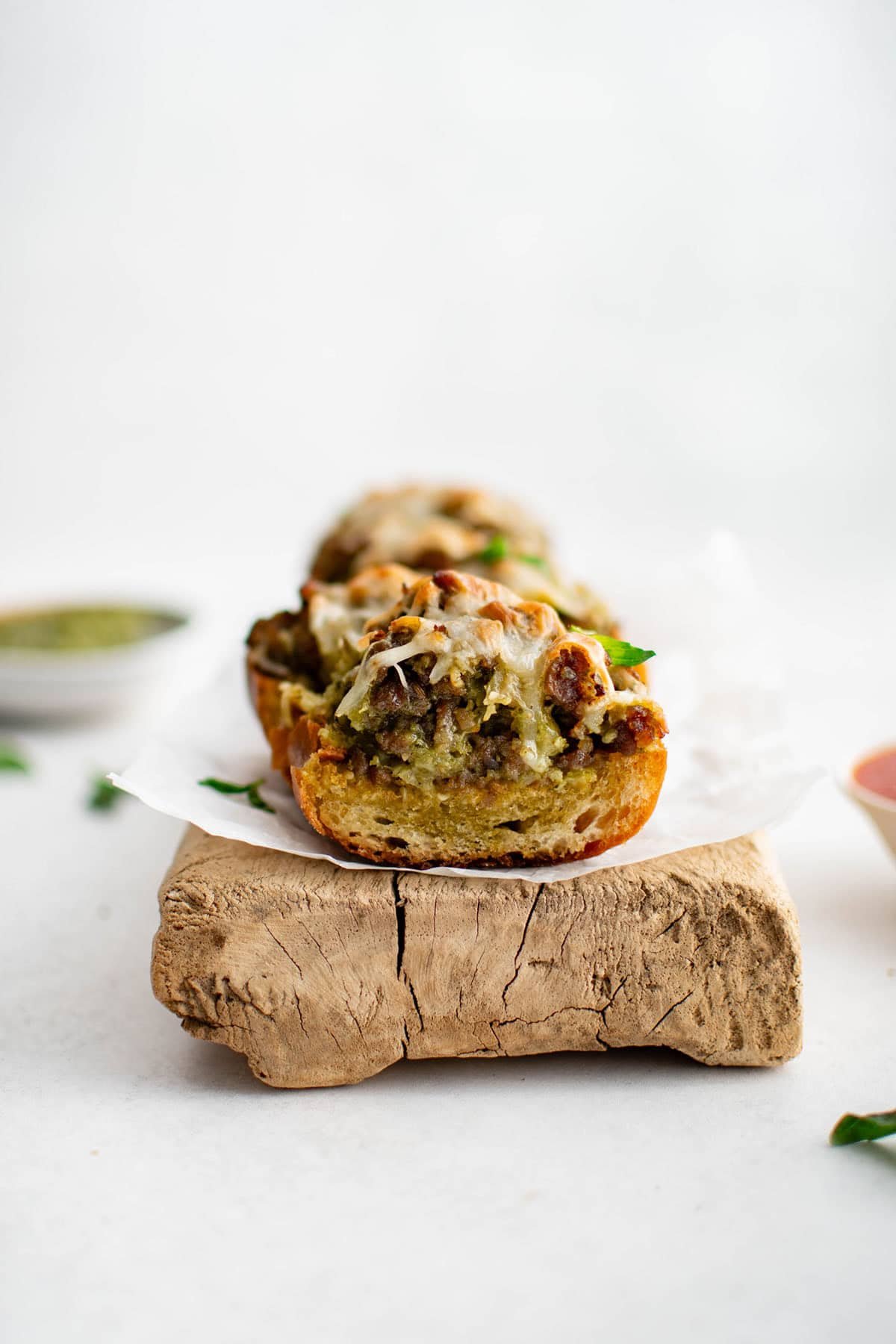 sausage pesto garlic bread on a serving platter. The image is from the side and the rich textures of the garlic breat, sausage pesto mixture, and cheese are all melded together.