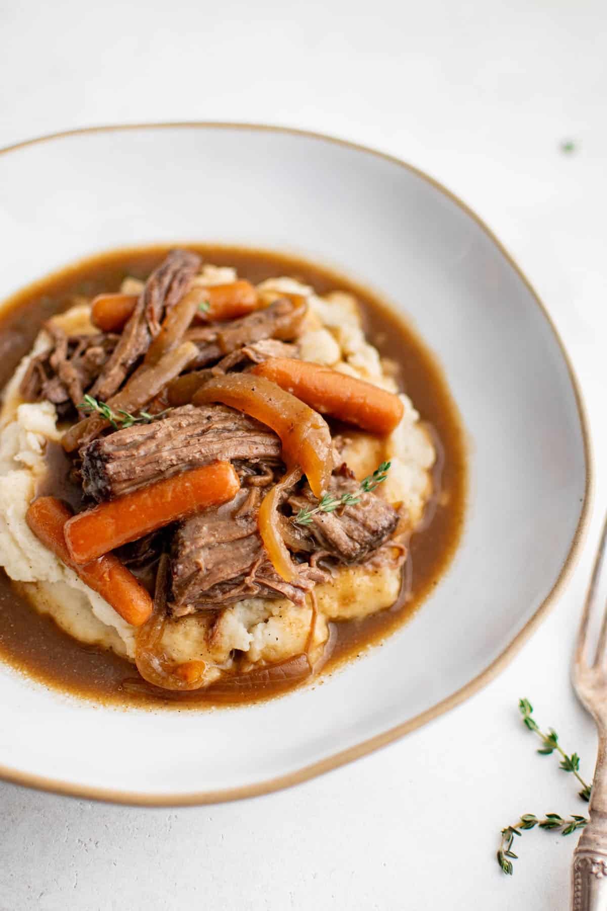slow cooker pot roast on a plate with carrots, mashed potatoes, and brown gravy