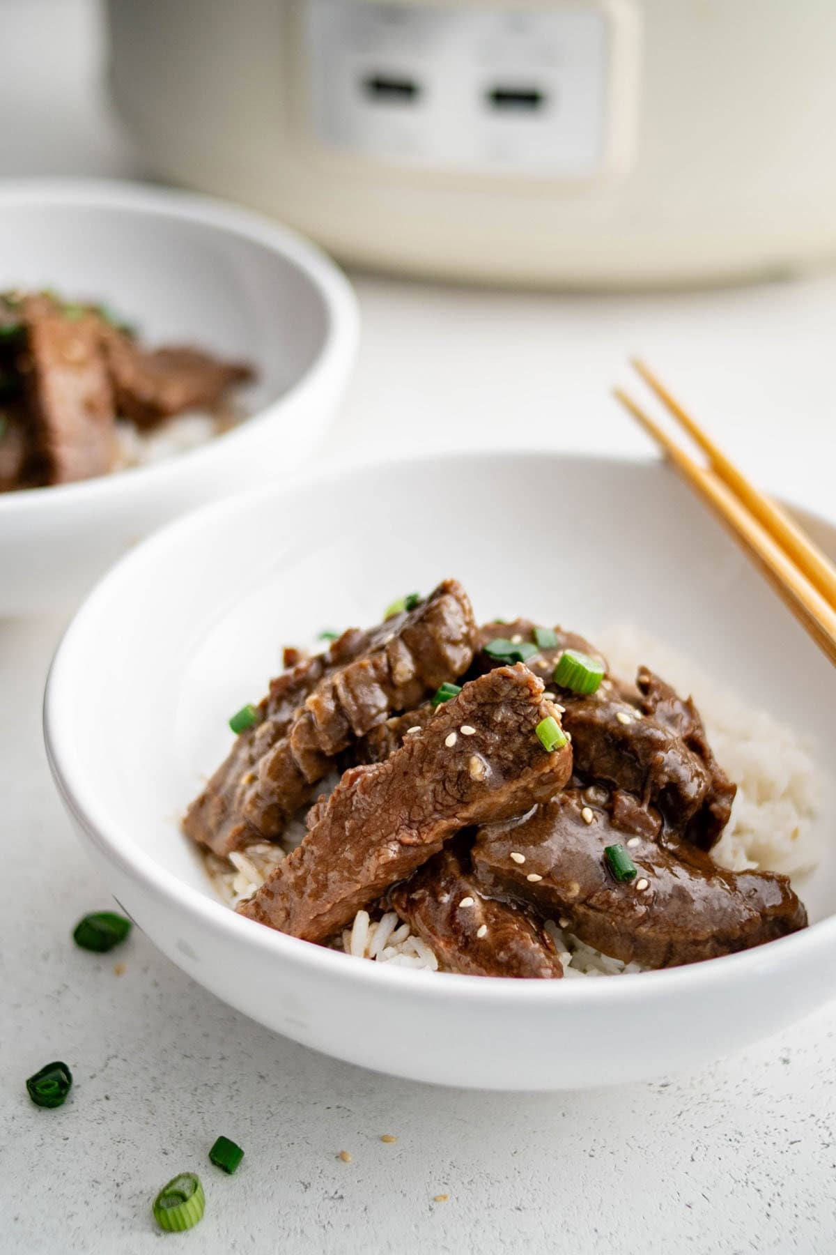 crockpot sesame beef over rice in a bowl with a pair of chop sticks