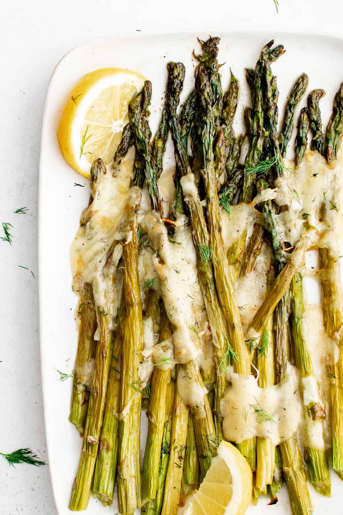 cheesy baked asparagus garnished with a slice of lemon on a serving platter