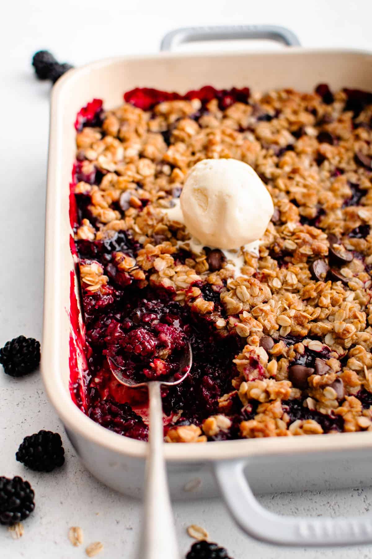 Blackberry Crisp with Chocolate Chip Oatmeal Crumble in a casserole dish with a dollop of vanilla ice cream