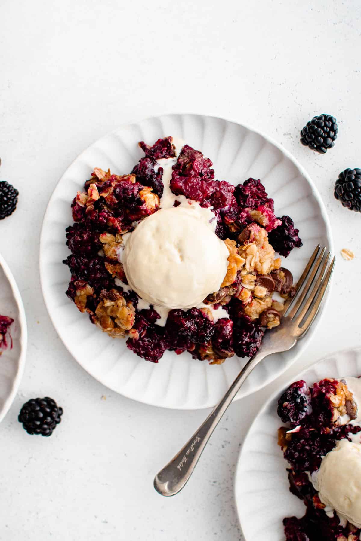 Blackberry Crisp with Chocolate Chip Oatmeal Crumble on a plate with a fork and a dollop of vanilla ice cream.