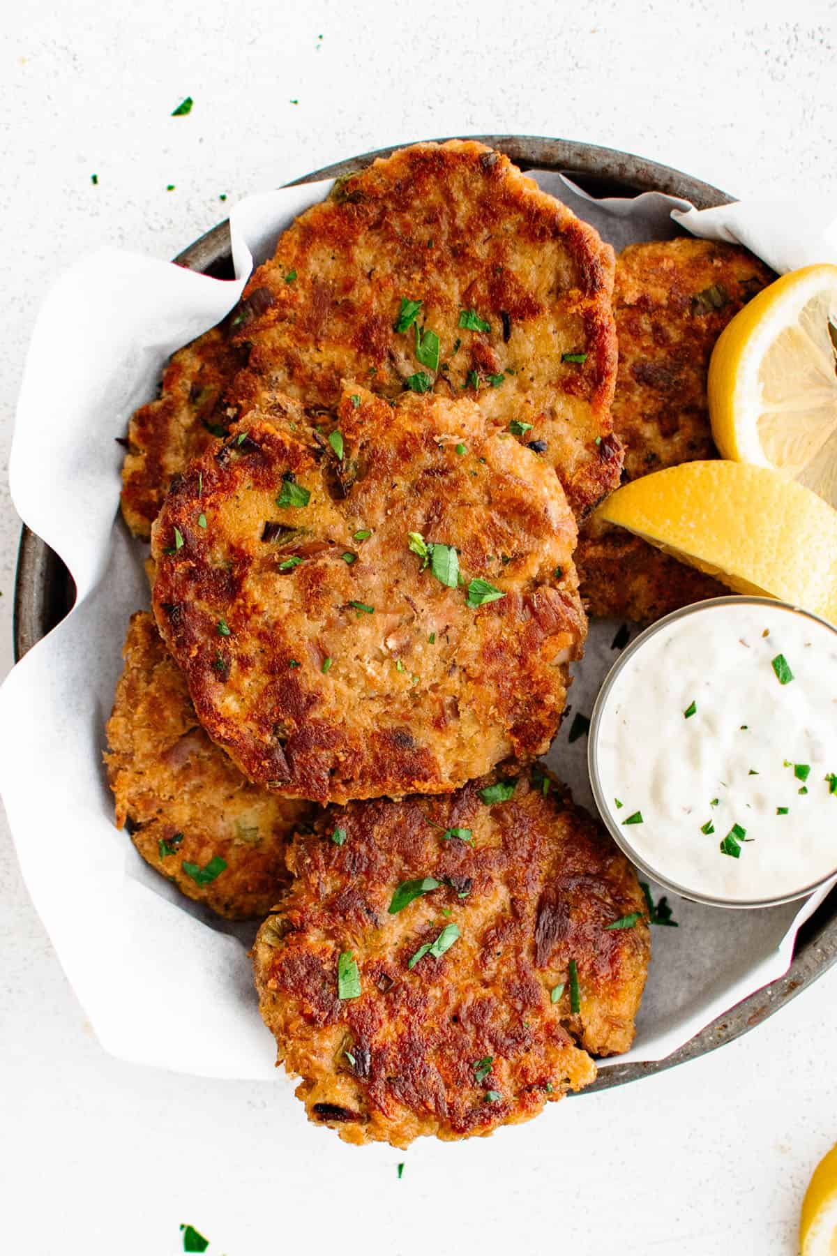 tuna patties on a plate with lemon wedges and tartar sauce
