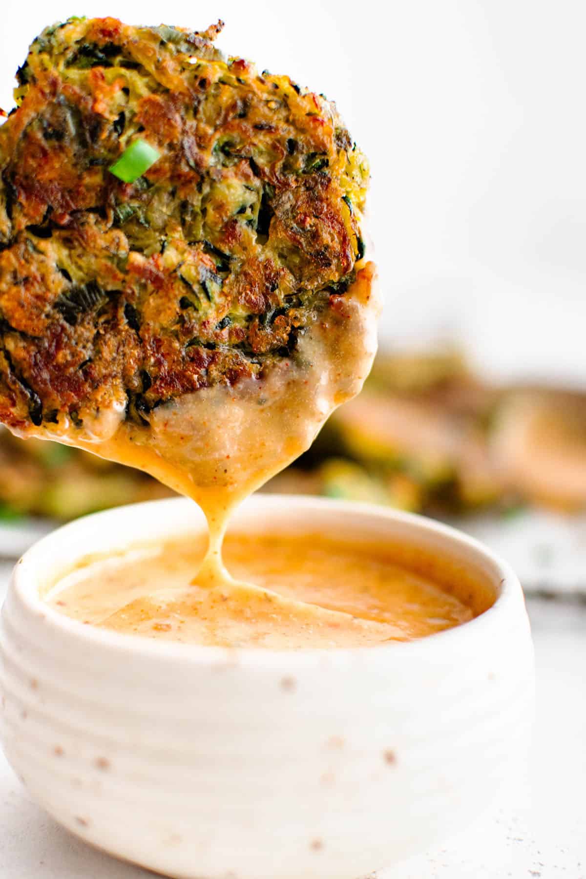 a zucchini fritter being dipped into the homemade cajun seasoned sauce