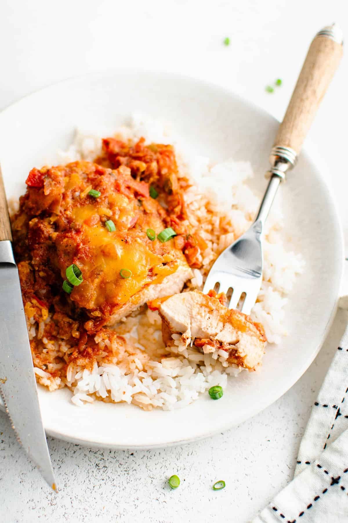 baked salsa chicken over rice on a plate with a fork holding a cut off bite of the chicken so the perfectly cooked texture of the chicken can be seen