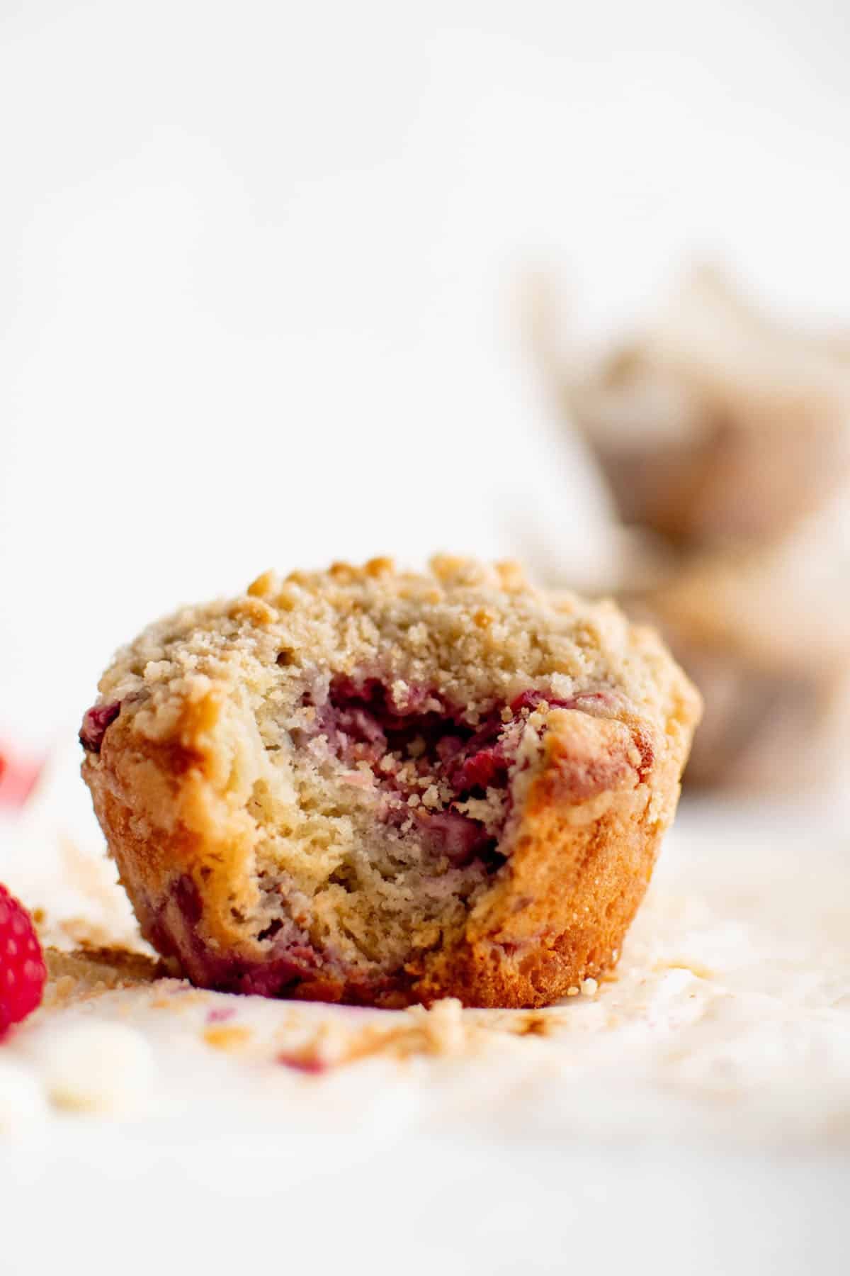 profile shot of a raspberry white chocolate muffin with a bite taken out of it, revealing the appetizing texture inside
