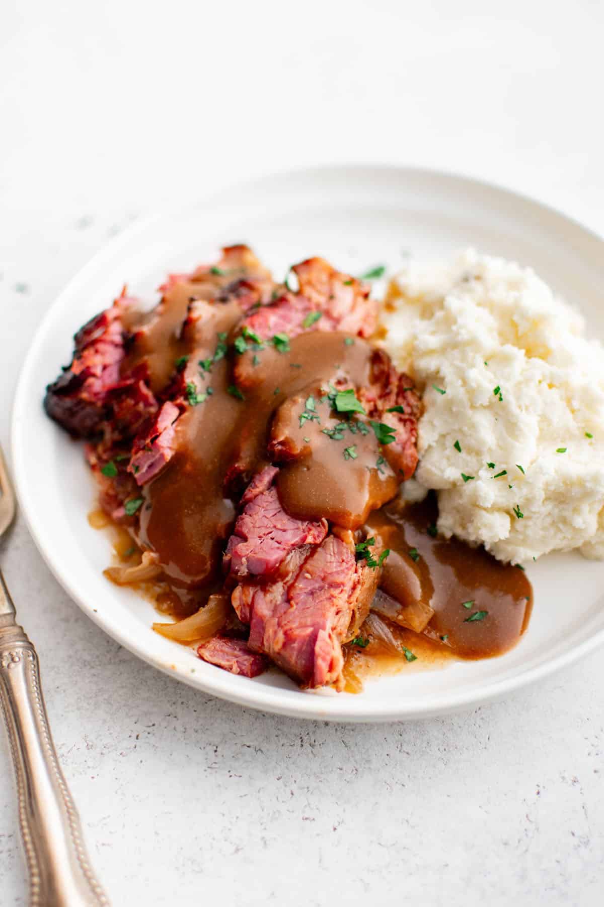 slices of slow cooker brisket on a plate with mashed potatoes and brown gravy