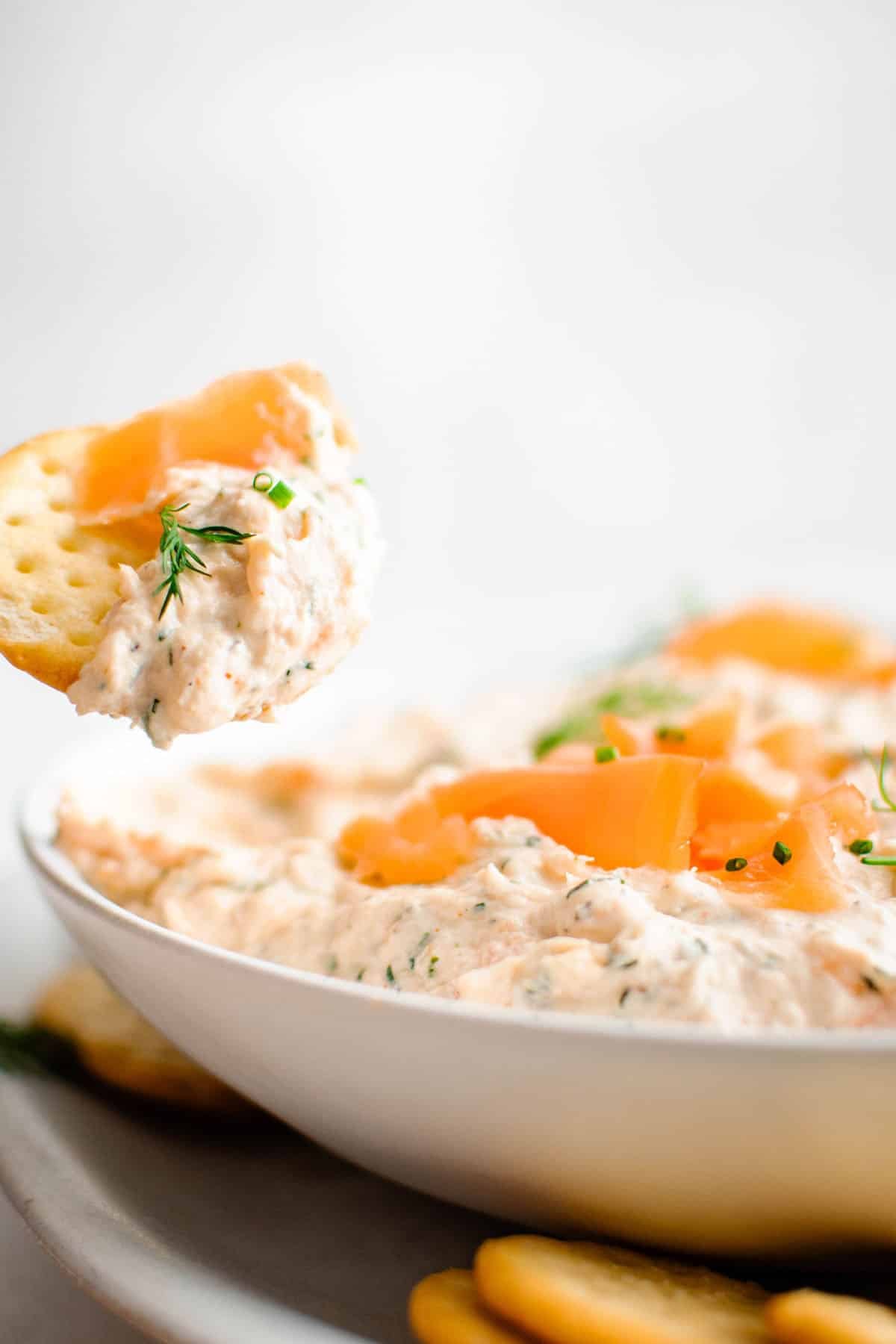 smoked salmon dip on a cracker that is over a bowl of smoked salmon dip