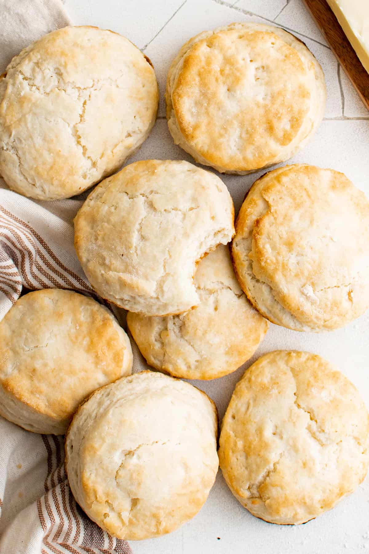 A pile of freshly baked 7 Up biscuits with a bite taken out of one so the flaky and fluffy texture inside can be seen