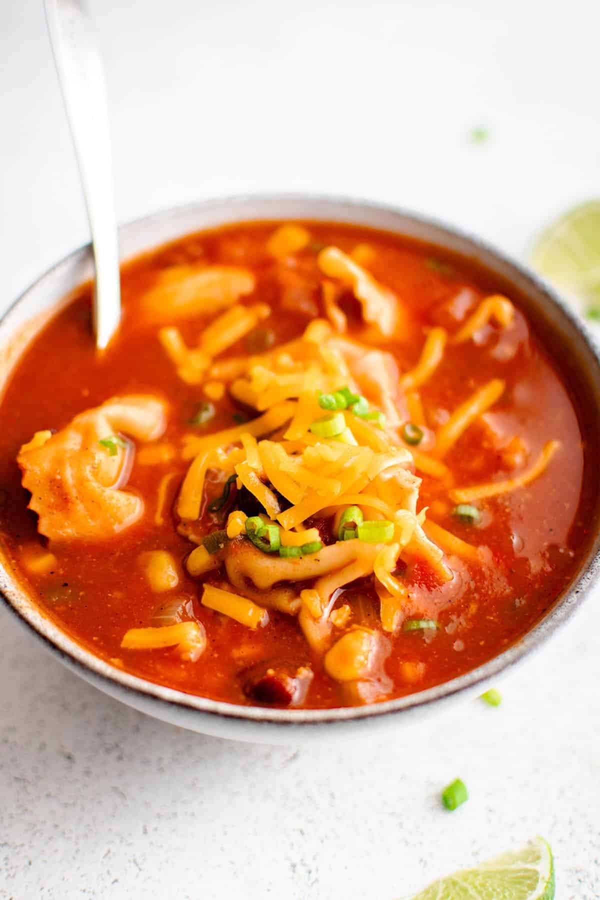 beef tortellini taco soup in a bowl with fresh cheddar and green onions emerging from the soup