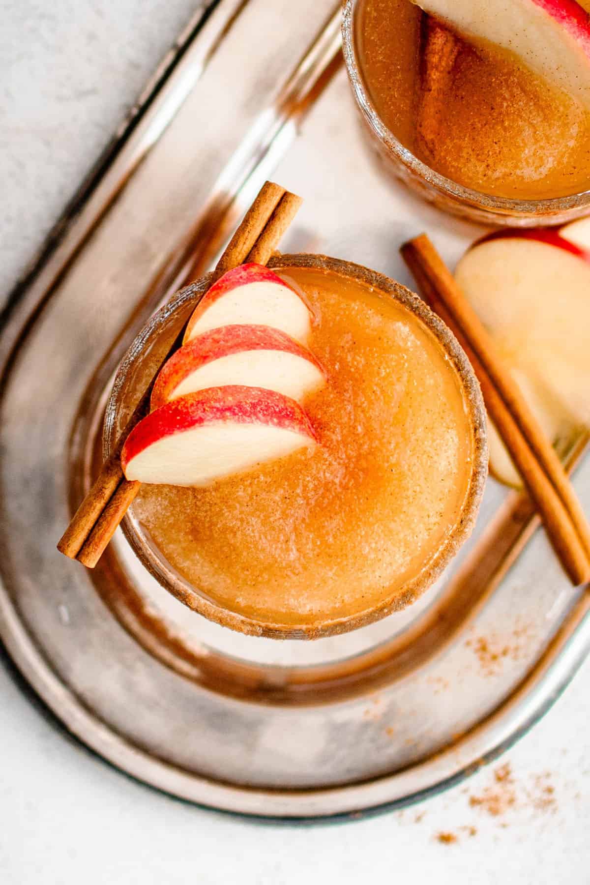 overhead photo of a frozen apple cider margarita garnished with thinly sliced apple and a cinnamon stick