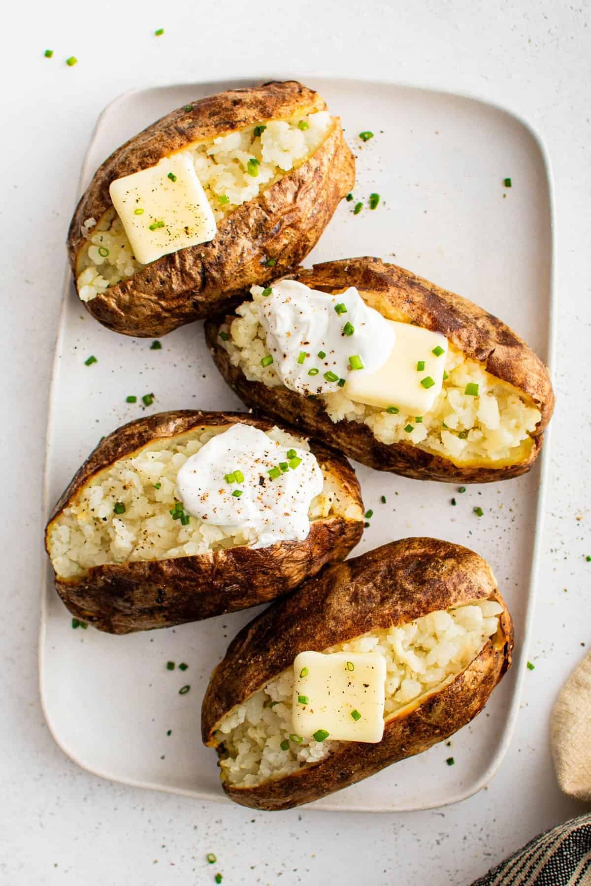 air fryer baked potatoes on a plate with butter, sour cream, and chives