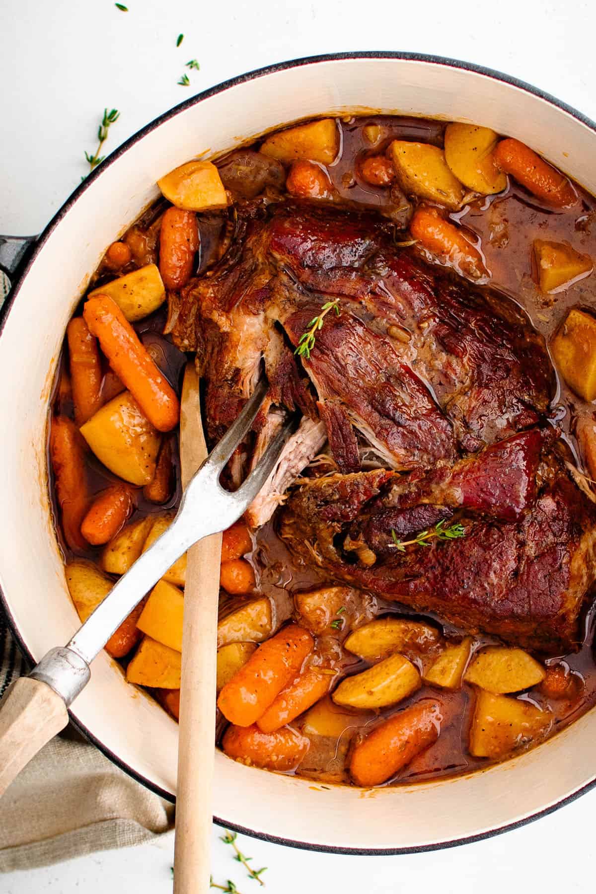 braised apple cider pork roast in a dutch oven with a wooden spoon and serving fork