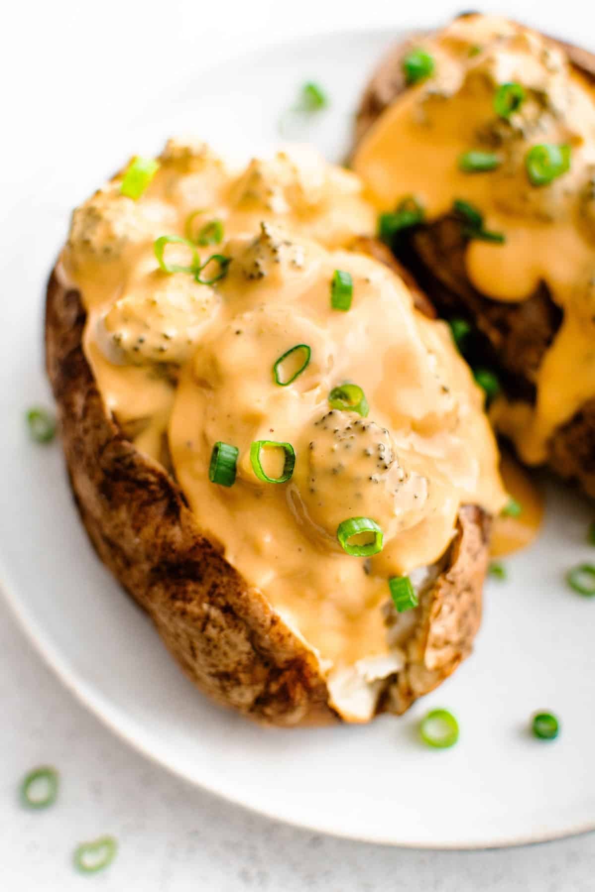 crockpot broccoli cheese sauce that has been poured over two baked potatoes and is slowly running down the sides of the potatoes, garnished with green onions