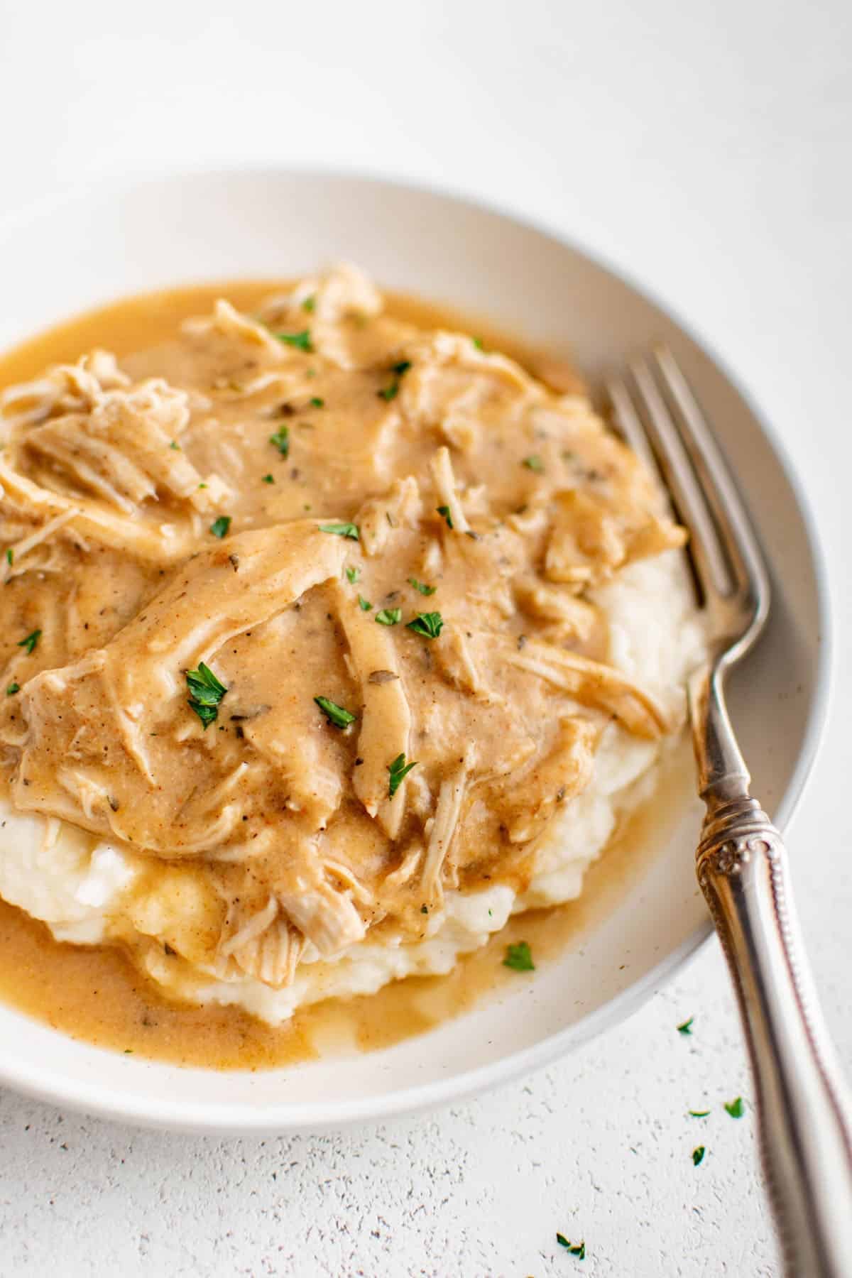 crockpot chicken and gravy atop a serving of mashed potatoes with a fork on a dinner plate