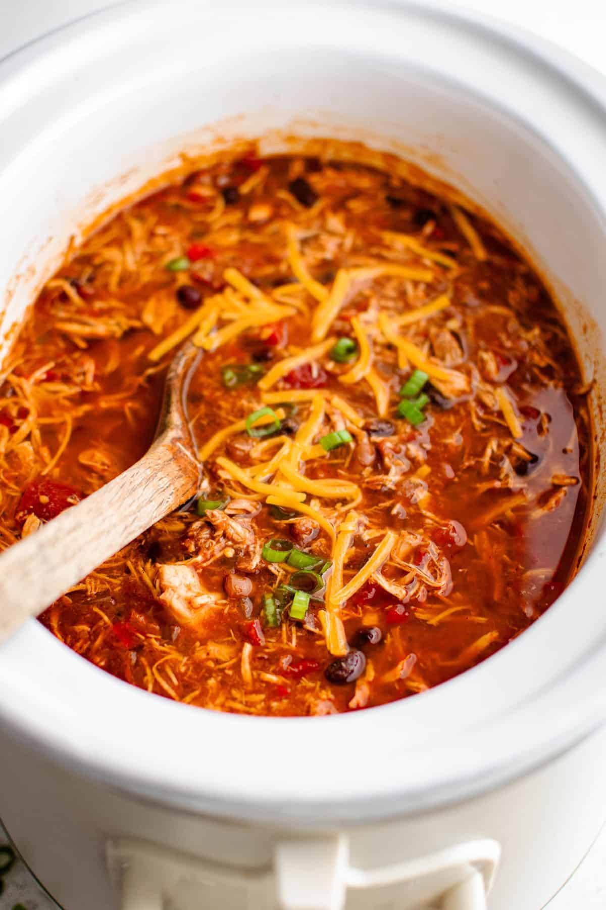 red chicken chili in a slow cooker garnished with green onions