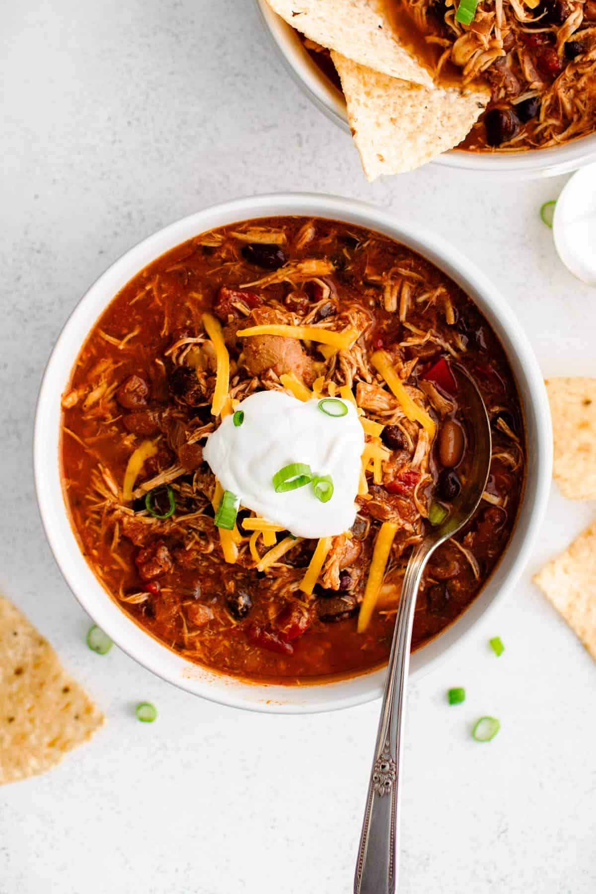 red chicken chili in a bowl with a dollop of sour cream and a green onion garnish